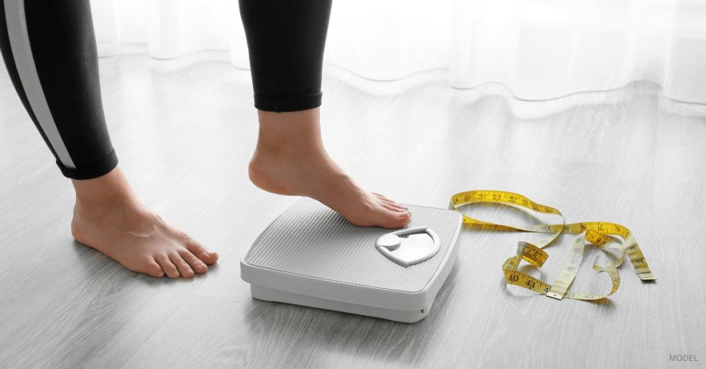 A woman's feet on a scale with a measuring tape discarded on the floor. (model)