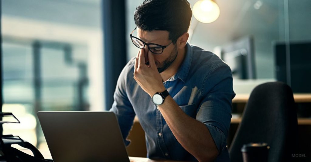 man at desk holding his face because he is tired (MODEL)