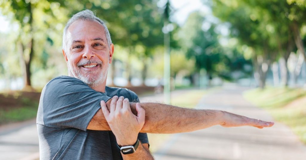 A middle aged man (model) enjoys working out and stretching in the park