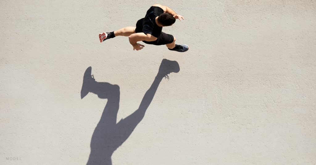 A man runs across concrete and his figure casts a shadow.